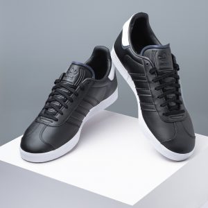 Two pairs of black Adidas trainers side by side, product photography