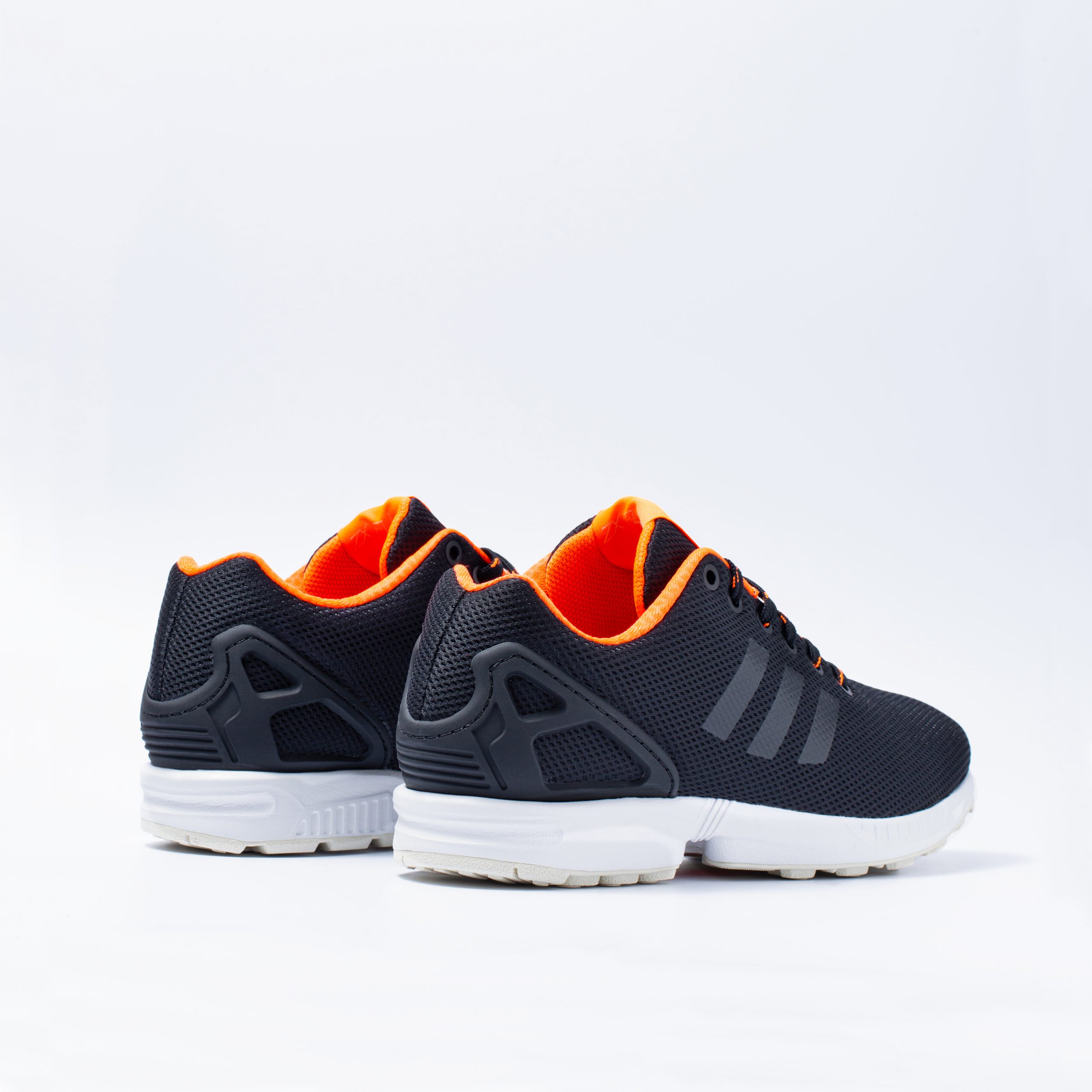 Adidas ZX Flux trainers in navy and orange viewed head-on from behind